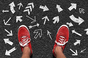 Person steht auf mehreren Richtungspfeilen als Symbol für Coaching-Entscheidungen und Wahlmöglichkeit