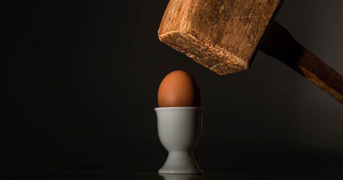 Ein großer Holzhammer schlägt auf ein Ei
