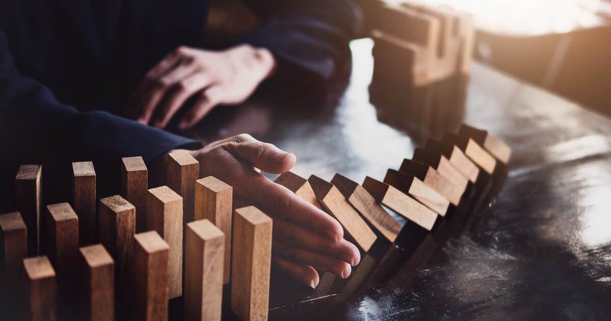 Hand stoppt fallende Dominosteine und symbolisiert das Eingreifen einer Wirtschaftsmediation zur Vermeidung eskalierender Konflikte.
