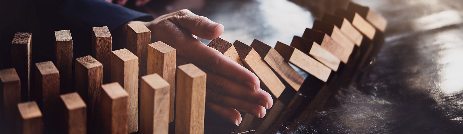 Hand stoppt fallende Dominosteine – Symbol für Wirtschaftsmediation, die Konflikte und Verluste verhindert
