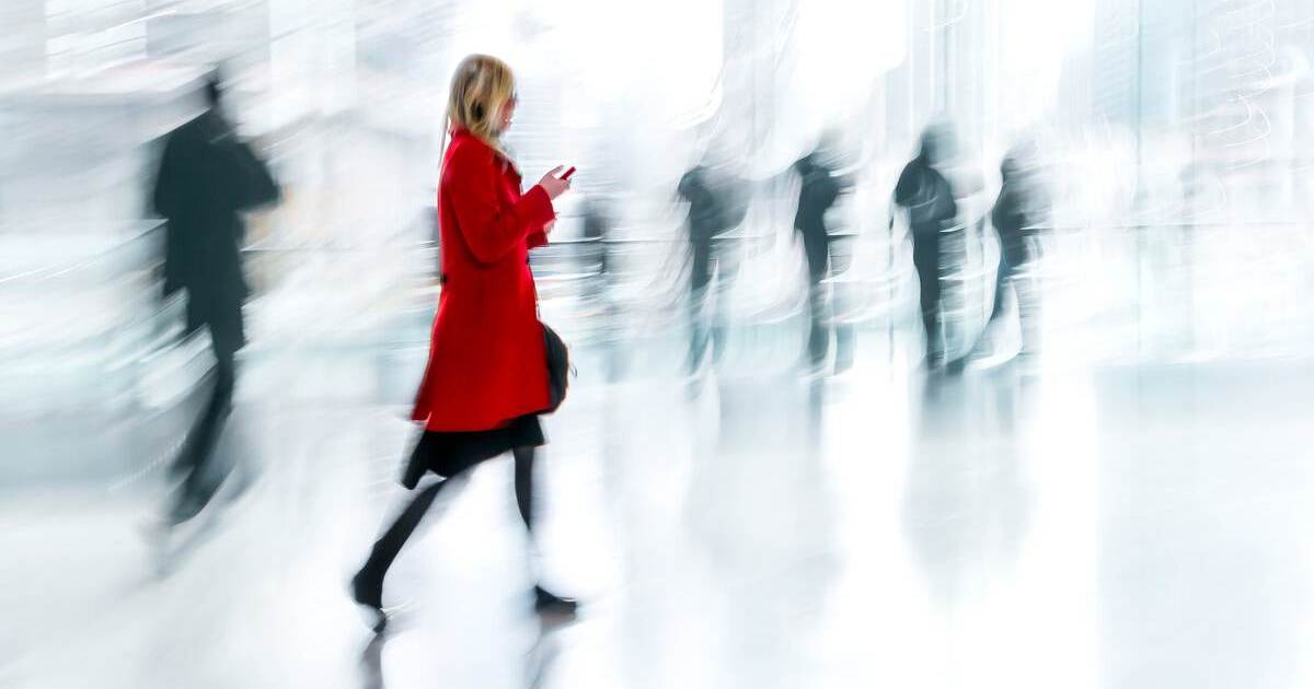 Reife Frau in auffälliger Jacke bewegt sich selbstbewusst vor einer Gruppe von Männern im grauen Business-Anzug bei einem Inhouse-Seminar zur Frauenförderung